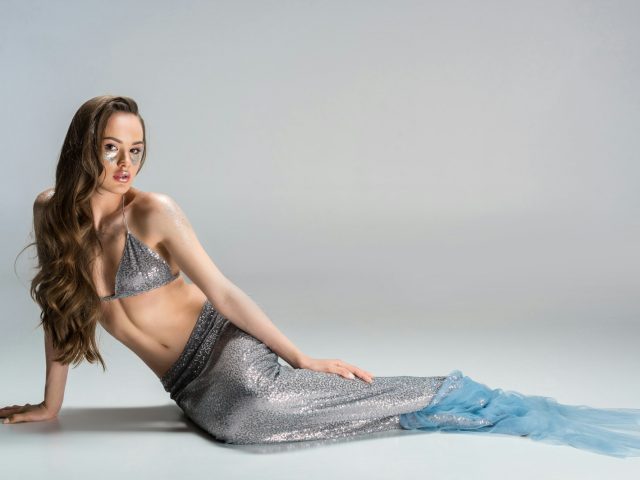 beautiful woman with mermaid tail lying on floor and looking at camera