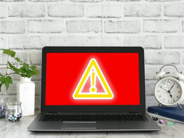 Computer screen showing red screen with yellow glowing danger sign. Concept hack virus cyber attack