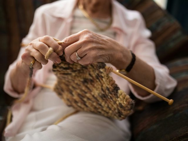 Midsection of senior woman knitting wool while sitting on sofa