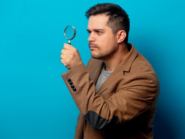 Surprised man with magnifying glass on blue background